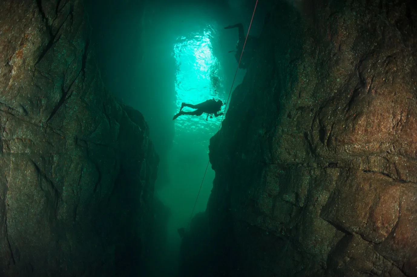 A diver silhouetted against green light in a narrow sea cave